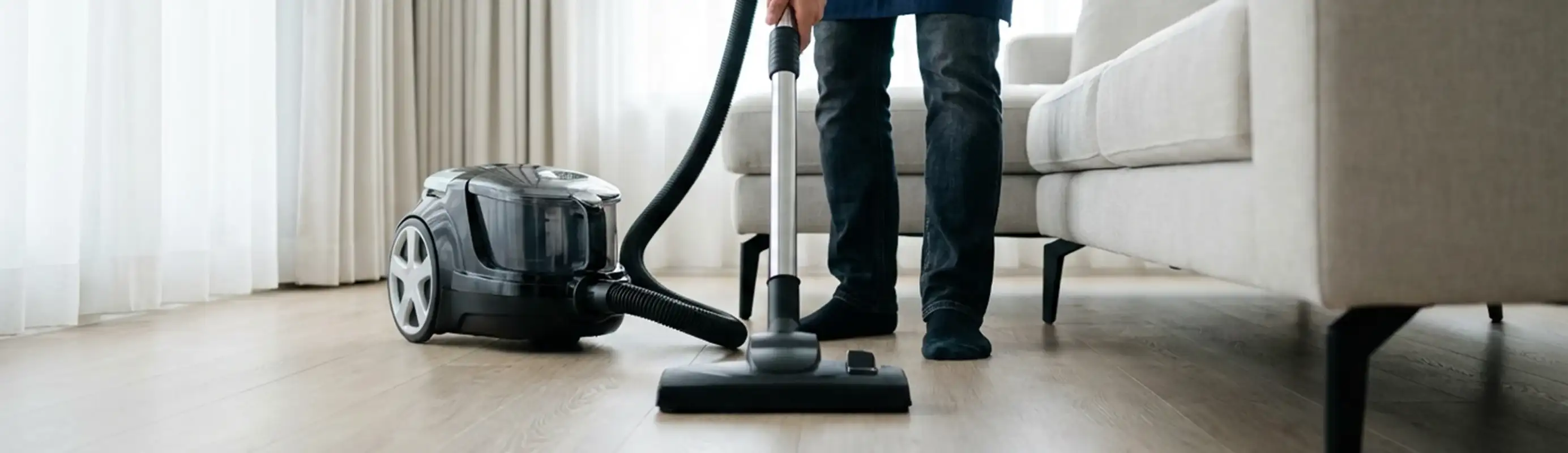 Professional house cleaner vacuuming a living room floor with a canister vacuum cleaner, Memphis, TN.