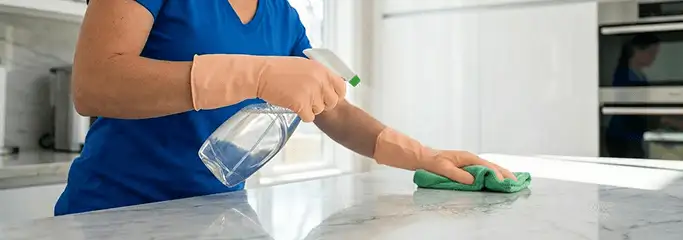 Maid service worker spraying and wiping a kitchen countertop with a microfiber cloth for sanitizing, Memphis, TN.