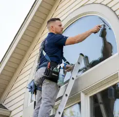 Professional window cleaner on a ladder using a squeegee to clean an exterior arched window, Memphis, TN.