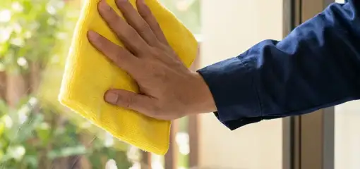 House cleaner wiping a glass window with a yellow microfiber cloth for streak-free cleaning, Memphis, TN.